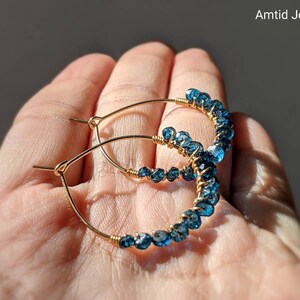 May include: Gold hoop earrings with blue topaz gemstones. The earrings are wire wrapped and have a delicate, bohemian style.