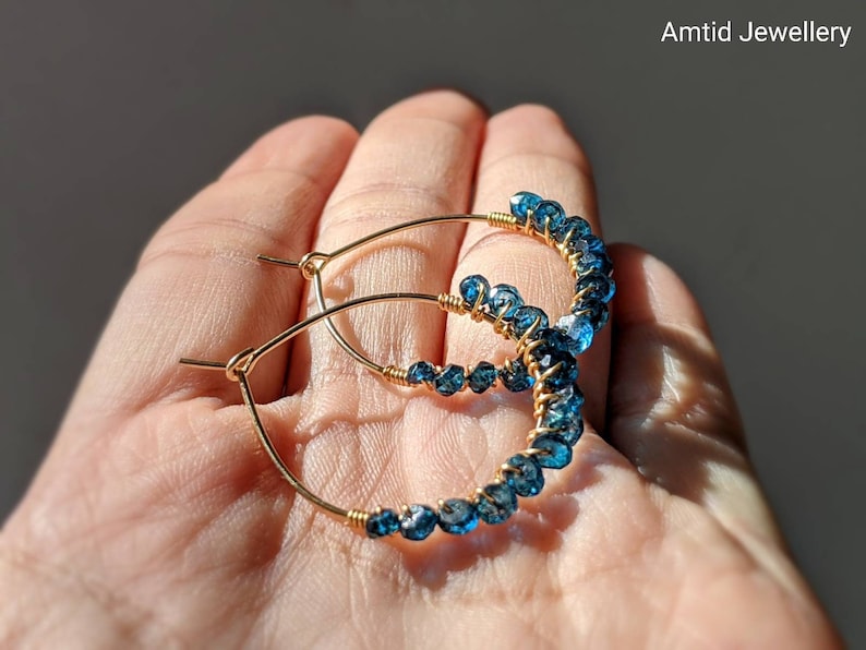May include: Gold hoop earrings with blue topaz gemstones. The earrings are wire wrapped and have a delicate, bohemian style.