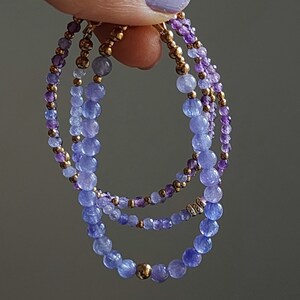 May include: Three layered bracelets with purple and blue gemstone beads and gold accents.