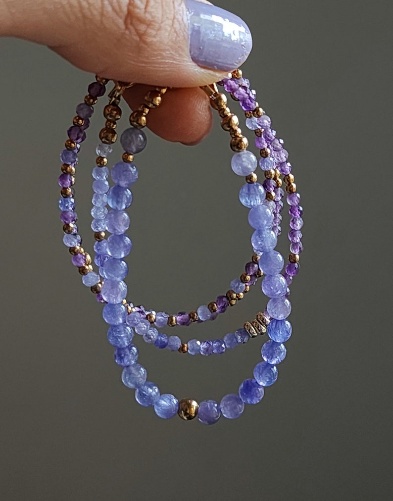 May include: Three layered bracelets with purple and blue gemstone beads and gold accents.