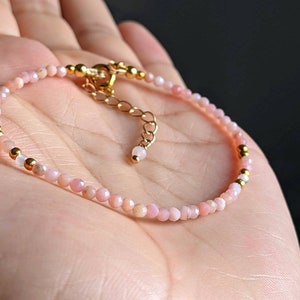 May include: A delicate pink opal and gold bead bracelet. The bracelet is made with small, round beads and has a gold clasp.