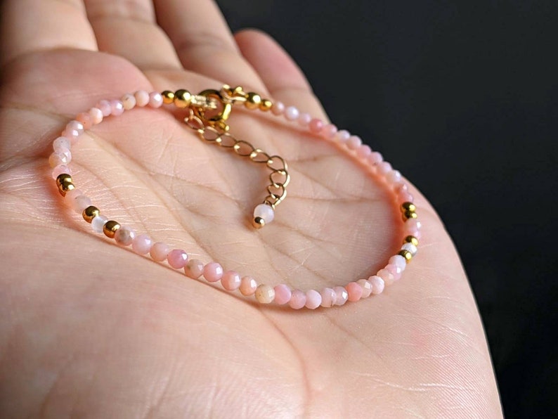 May include: A delicate pink opal and gold bead bracelet. The bracelet is made with small, round beads and has a gold clasp.