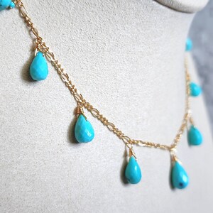 May include: A delicate gold chain necklace featuring teardrop-shaped turquoise beads. The necklace has a delicate chain design with multiple turquoise pendants, creating a layered effect. The turquoise beads are a vibrant blue-green color.