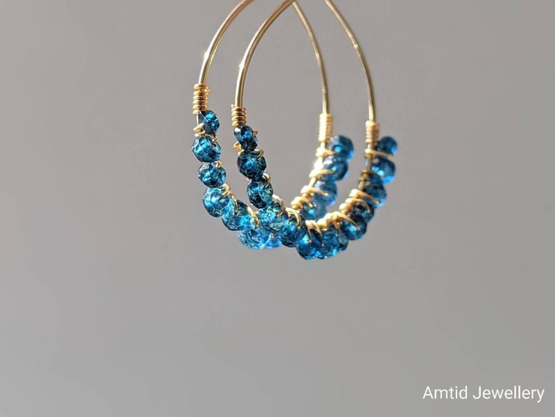 May include: Gold hoop earrings with blue gemstone beads. The earrings are made of wire and have a delicate, minimalist design.