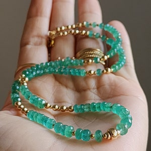 May include: A green emerald gemstone necklace with gold beads. The necklace is layered and has a delicate look.