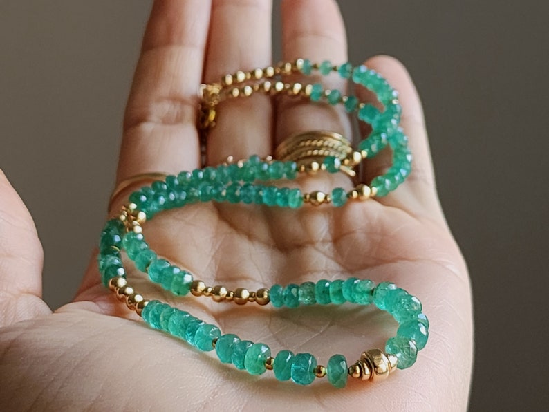 May include: A green emerald gemstone necklace with gold beads. The necklace is layered and has a delicate look.