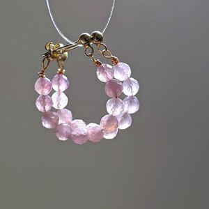 May include: A pair of pink gemstone hoop earrings with a gold wire and clasp. The earrings are made of small, round beads.