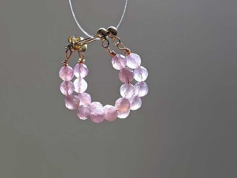 May include: A pair of pink gemstone hoop earrings with a gold wire and clasp. The earrings are made of small, round beads.