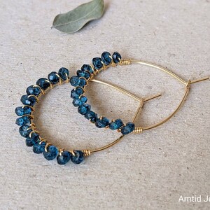 May include: Gold hoop earrings with blue gemstone beads. The earrings are made with wire wrapped around the beads.