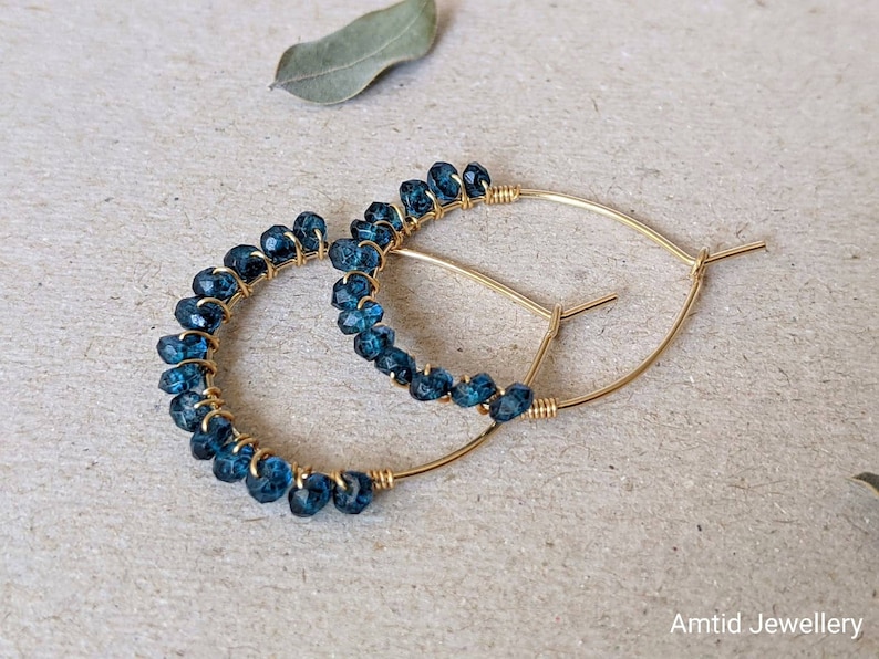 May include: Gold hoop earrings with blue gemstone beads. The earrings are made with wire wrapped around the beads.