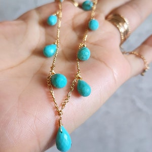 May include: A delicate gold necklace featuring turquoise beads in various shapes. The necklace has a chain design with small round and teardrop-shaped turquoise stones. The gold chain is visible, and the necklace is displayed against a neutral background.
