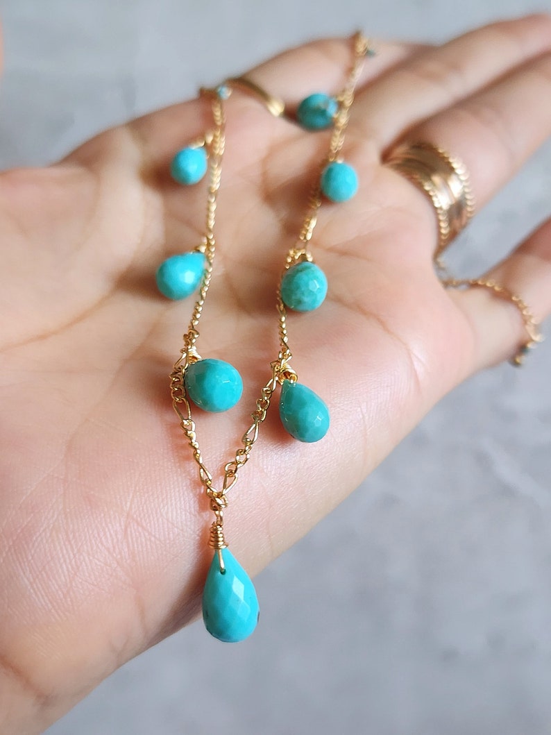 May include: A delicate gold necklace featuring turquoise beads in various shapes. The necklace has a chain design with small round and teardrop-shaped turquoise stones. The gold chain is visible, and the necklace is displayed against a neutral background.