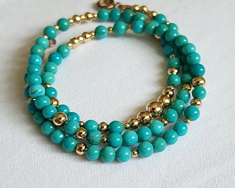 May include: A triple-strand turquoise and gold bead bracelet. The bracelet features turquoise beads of varying sizes and gold beads interspersed throughout.