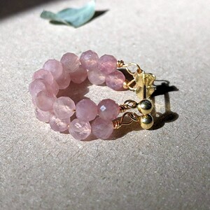 May include: A pair of pink gemstone hoop earrings with gold wire and gold bead accents.