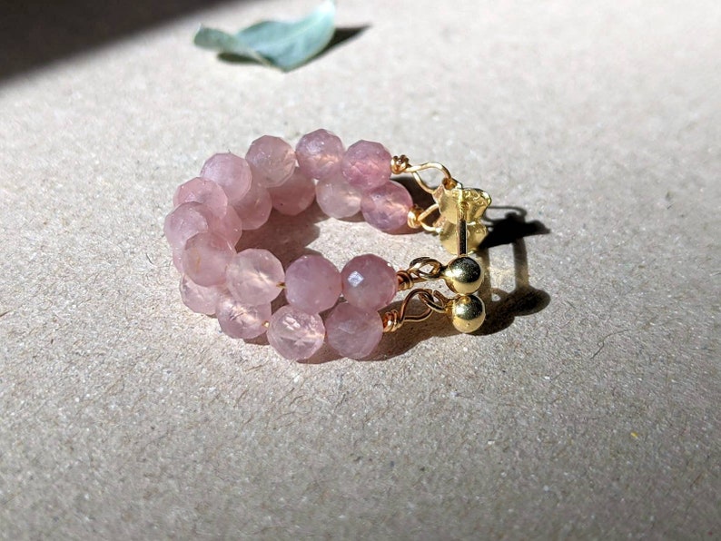 May include: A pair of pink gemstone hoop earrings with gold wire and gold bead accents.