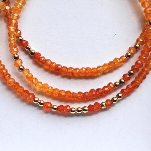 May include: Three strands of orange gemstone necklaces with gold-colored beads. The necklaces are made of small, faceted beads in shades of orange and yellow. The gold beads are evenly spaced along the strands, adding a touch of elegance.