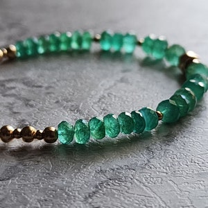 May include: A green gemstone bracelet with gold beads. The bracelet is made of small, faceted gemstones and gold beads.