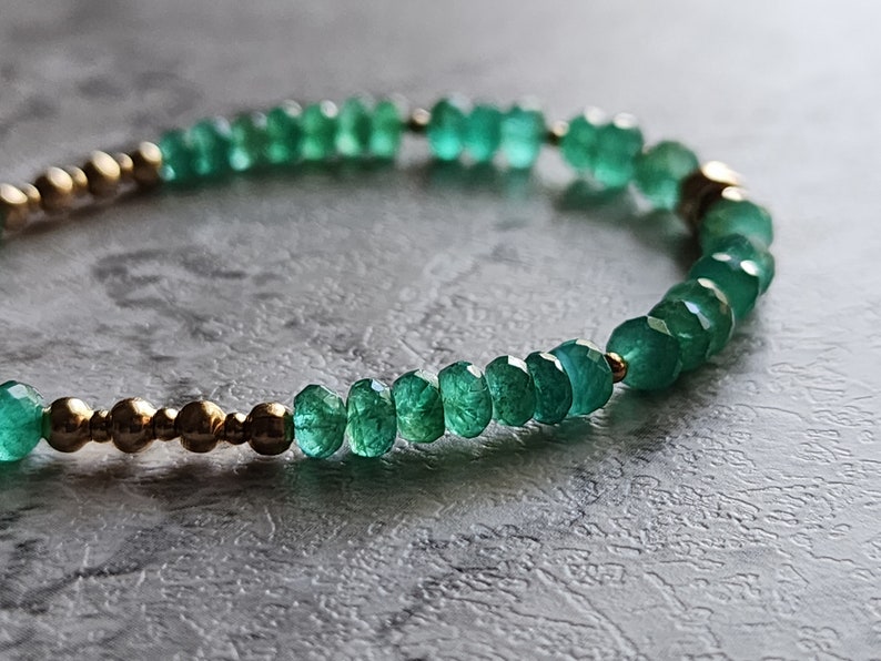 May include: A green gemstone bracelet with gold beads. The bracelet is made of small, faceted gemstones and gold beads.