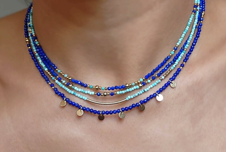 May include: A layered necklace with blue and turquoise beads and gold accents. The necklace has small gold discs hanging from the bottom.