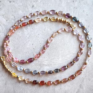 Op de afbeelding: Een veelkleurige edelsteenketting met ovale kralen in tinten roze, blauw en groen. De ketting is gemaakt van goudkleurig metaal en heeft een sluiting.
