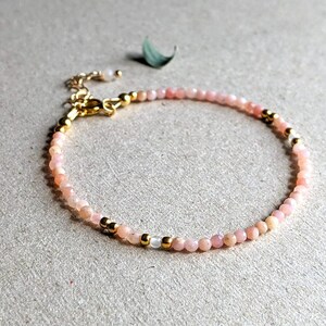 May include: A delicate bracelet made with small pink opal beads and gold accents.