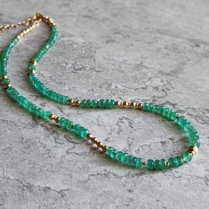May include: A delicate gold chain necklace with green gemstone beads. The necklace is made of small, round beads that are strung together to create a simple and elegant design.