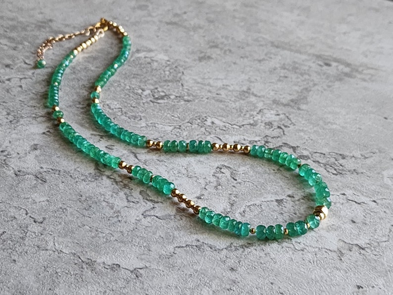 May include: A delicate gold chain necklace with green gemstone beads. The necklace is made of small, round beads that are strung together to create a simple and elegant design.