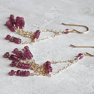 Puede incluir: Pendientes de oro con una cadena colgante y m&uacute;ltiples hebras de peque&ntilde;as cuentas de color rosa oscuro.