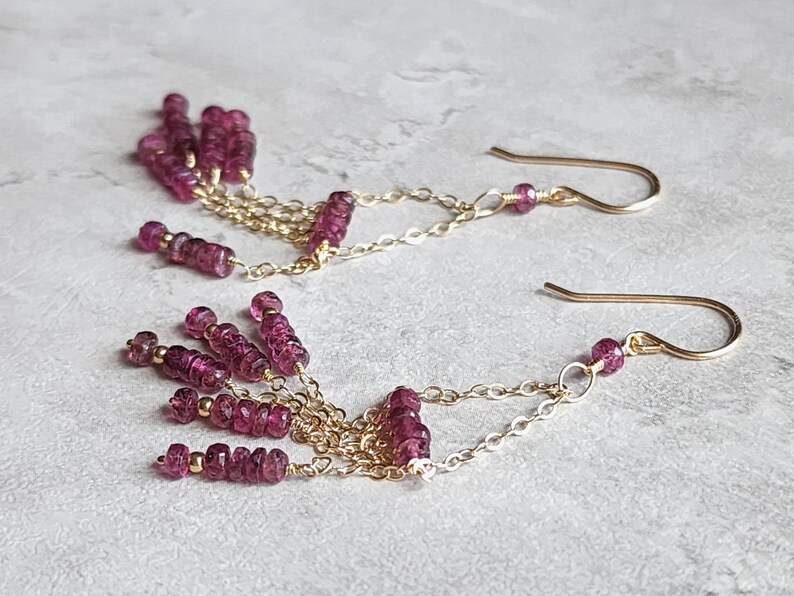 Puede incluir: Pendientes de oro con una cadena colgante y m&uacute;ltiples hebras de peque&ntilde;as cuentas de color rosa oscuro.