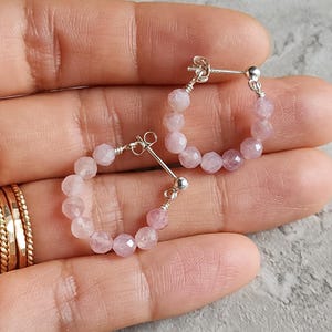 May include: A pair of silver hoop earrings with pink gemstone beads. The earrings are small and delicate.