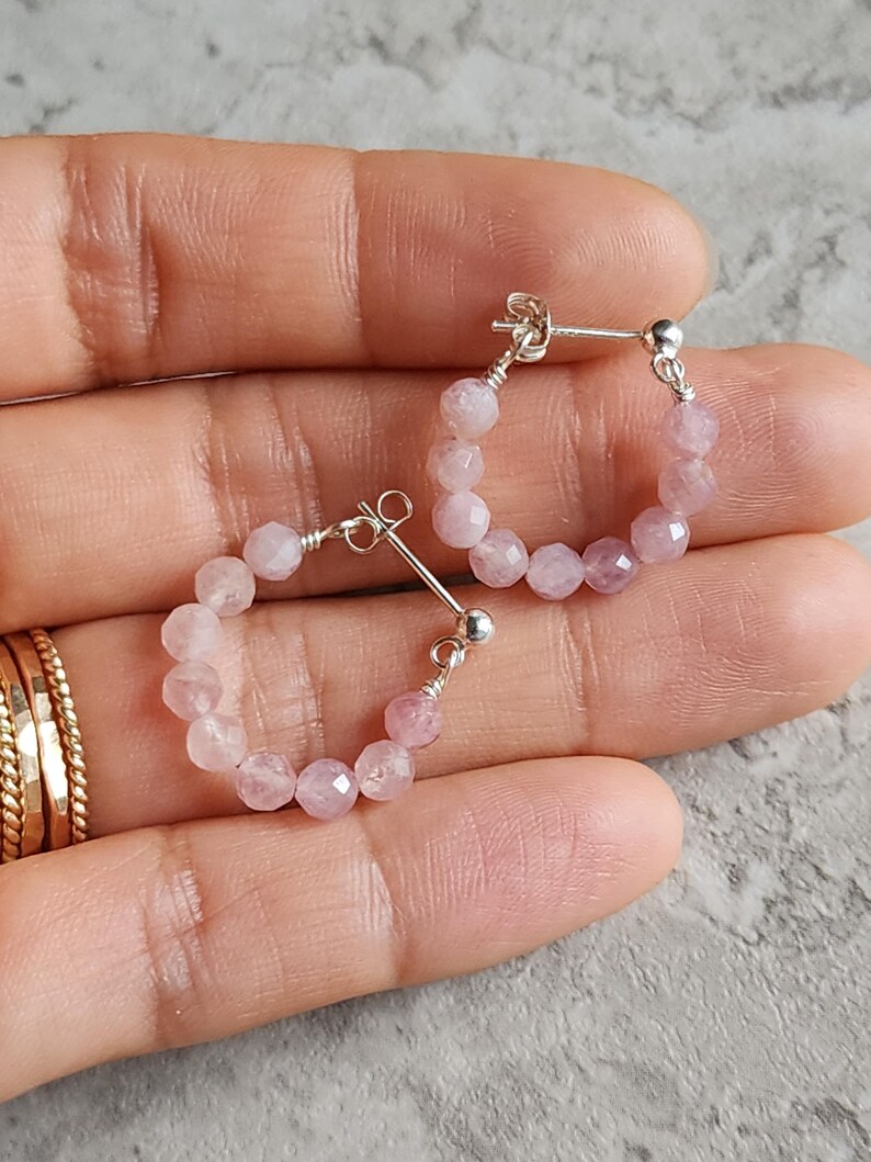 May include: A pair of silver hoop earrings with pink gemstone beads. The earrings are small and delicate.