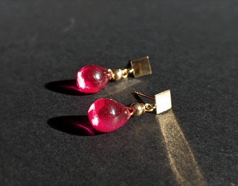 May include: A pair of gold earrings with teardrop-shaped red glass stones.