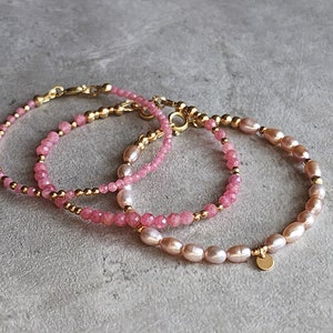 Puede incluir: Tres pulseras delicadas con piedras rosas y perlas. Las pulseras presentan cuentas y cierres dorados. Una pulsera est&aacute; hecha de peque&ntilde;as piedras rosas facetadas, las otras tienen perlas rosas.