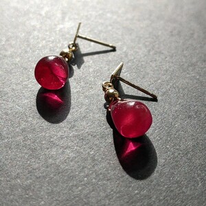 May include: A pair of earrings with red gemstone drops. The earrings have gold posts and are a simple and elegant design.