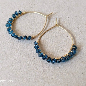 May include: Gold hoop earrings with blue gemstone beads. The earrings are made with wire and have a simple design.