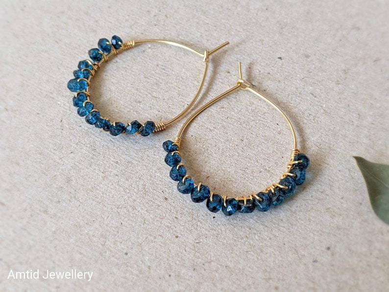 May include: Gold hoop earrings with blue gemstone beads. The earrings are made with wire and have a simple design.
