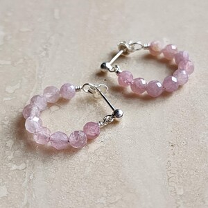 May include: A pair of silver hoop earrings with pink gemstone beads. The earrings are made with small, faceted beads that are strung together to form a circle.