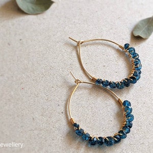 May include: A pair of gold hoop earrings with blue gemstone beads. The earrings are delicate and feminine.