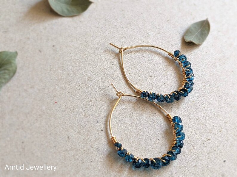 May include: A pair of gold hoop earrings with blue gemstone beads. The earrings are delicate and feminine.