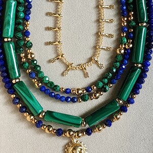 May include: A layered necklace with green malachite and blue lapis lazuli beads, gold chain with small charms, and a gold sun pendant.