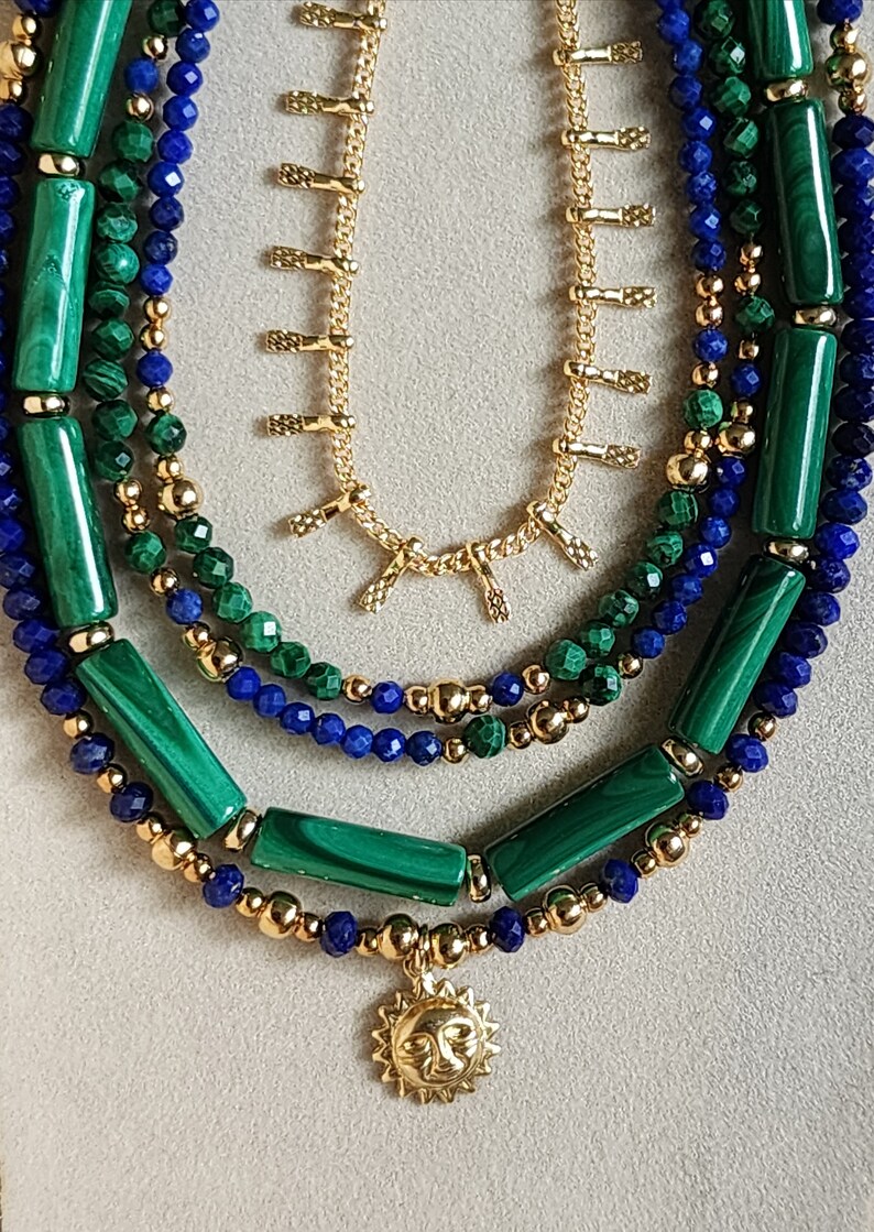 May include: A layered necklace with green malachite and blue lapis lazuli beads, gold chain with small charms, and a gold sun pendant.