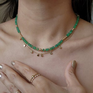 May include: A gold necklace with a delicate chain and a strand of green gemstone beads. The necklace has a pendant of small gold discs.