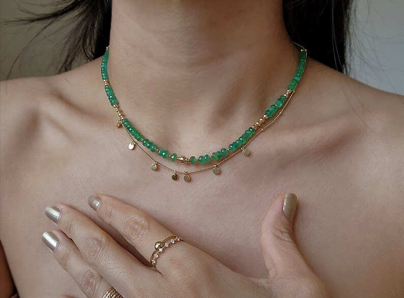 May include: A gold necklace with a delicate chain and a strand of green gemstone beads. The necklace has a pendant of small gold discs.