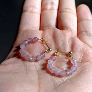 May include: A pair of hoop earrings made with small, light pink beads and gold accents.