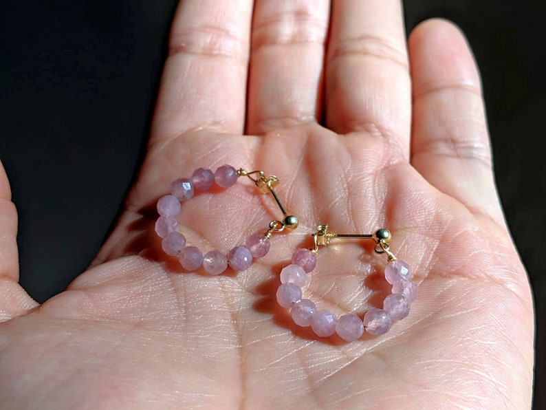 May include: A pair of hoop earrings made with small, light pink beads and gold accents.