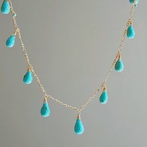 May include: A delicate gold necklace featuring turquoise teardrop-shaped beads. The necklace has a delicate chain with multiple turquoise beads dangling at intervals, creating a graceful and elegant design. The gold chain and turquoise beads create a beautiful contrast.