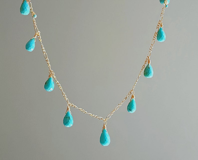 May include: A delicate gold necklace featuring turquoise teardrop-shaped beads. The necklace has a delicate chain with multiple turquoise beads dangling at intervals, creating a graceful and elegant design. The gold chain and turquoise beads create a beautiful contrast.