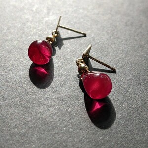 May include: A pair of gold earrings with red gemstone drops. The earrings have a simple design and are perfect for everyday wear.