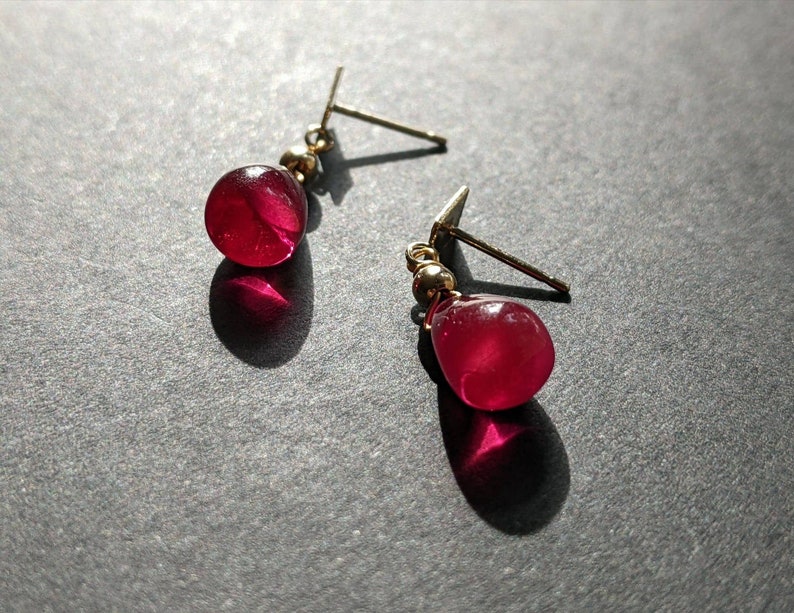 May include: A pair of gold earrings with red gemstone drops. The earrings have a simple design and are perfect for everyday wear.