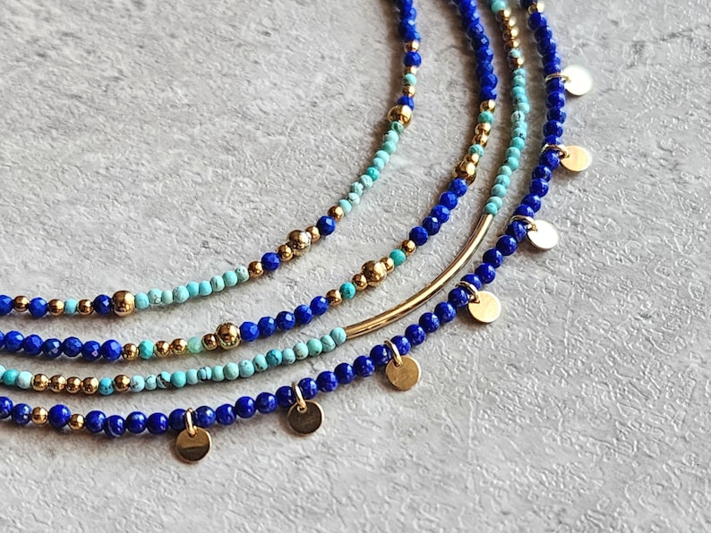 May include: A layered necklace with blue and turquoise beads and gold accents. The necklace features small gold discs hanging from the bottom.